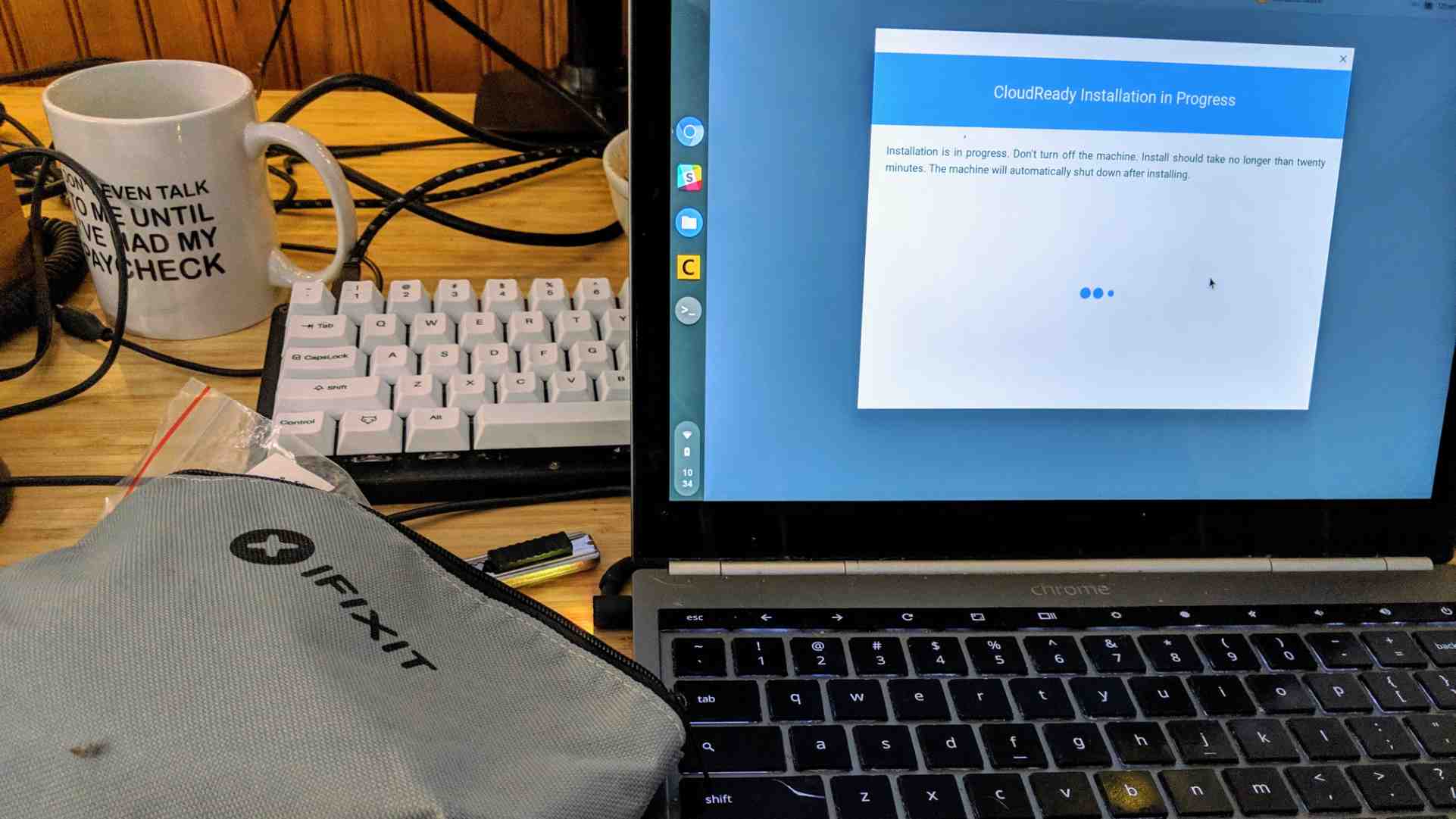 Chromebook Pixel showing the installation screen of CloudReady, next to a keyboard, coffee mug, and iFixit toolkit.