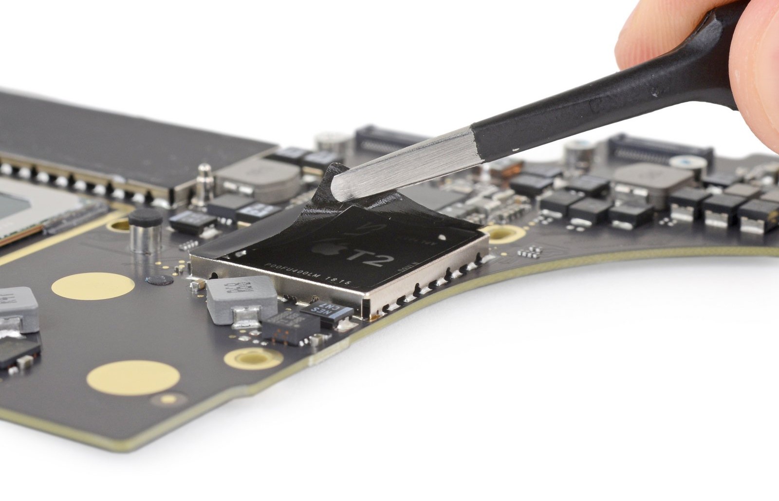 A pair of tweezers uncovering the T2 security chip on a MacBook Pro logic board.