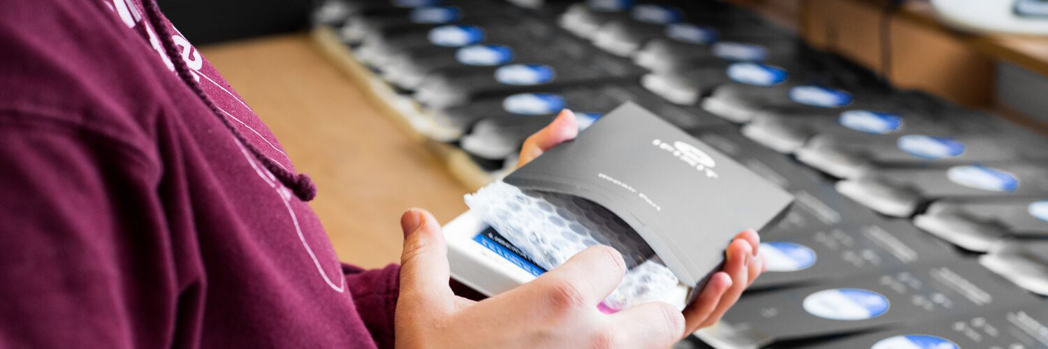 A person kitting an iFixit kit, inserting a replacement part into a box, more boxes are visible in the background.