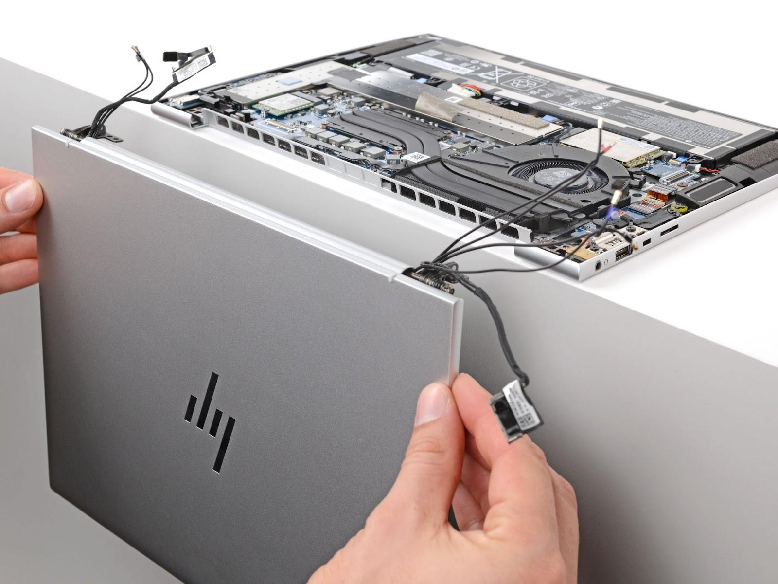 Ein HP EliteBook G9 hängt kopfüber an der Kante einer weißen Oberfläche. Die untere Abdeckung des Laptops ist entfernt worden. Zwei Hände ziehen das abgekoppelte Display vom Laptop weg.