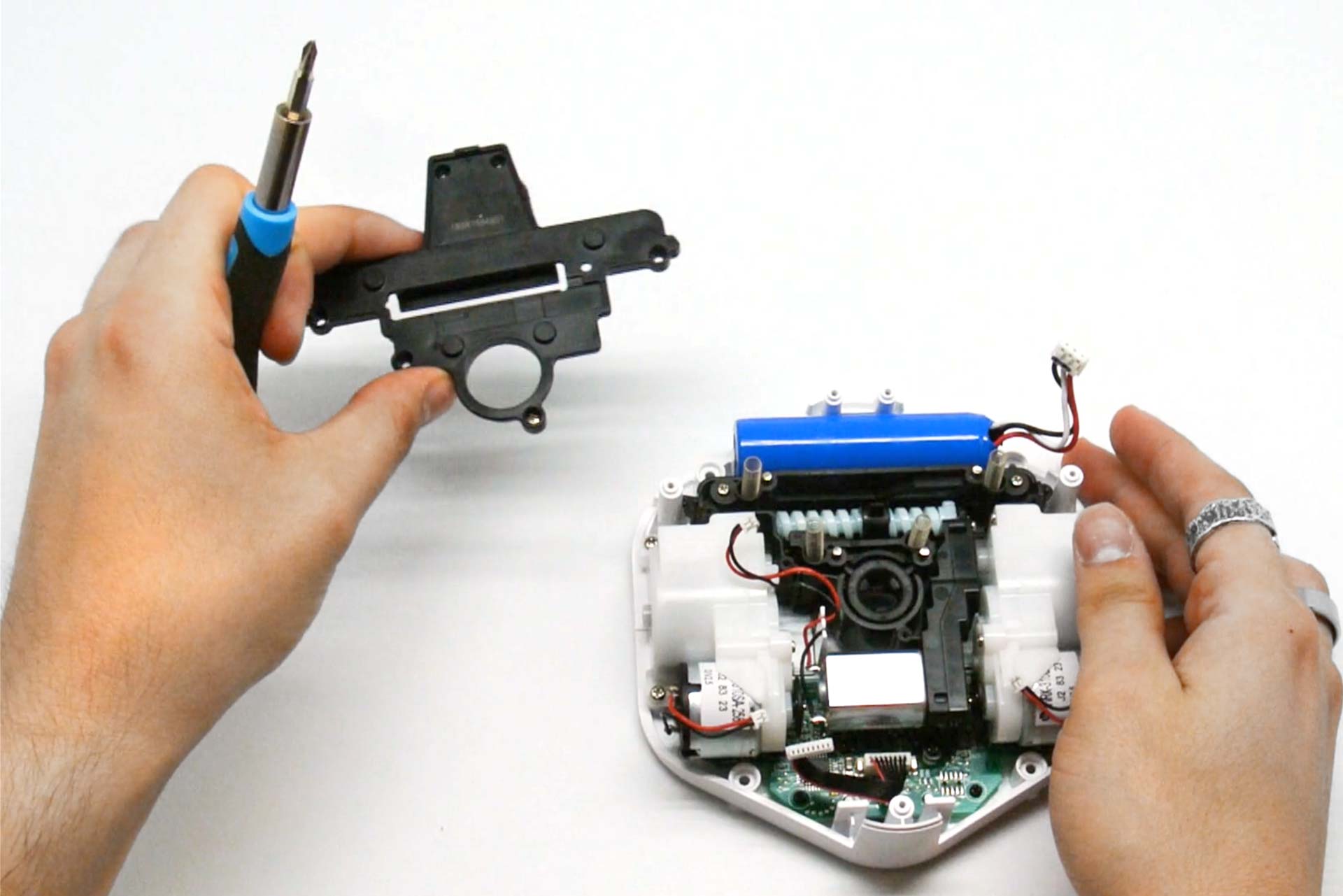 A robotics student uses a screwdriver to remove parts from a partially disassembled iRobot Root coding robot.