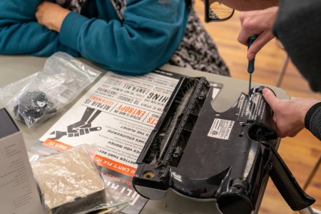 Someone using a screwdriver on a vacuum head on top of a repair manifesto at a repair cafe
